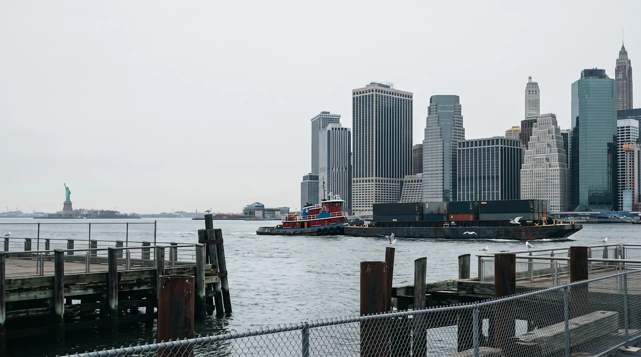 Lower Manhattan skyline across the harbor with the Statue of Liberty and a working tugboat